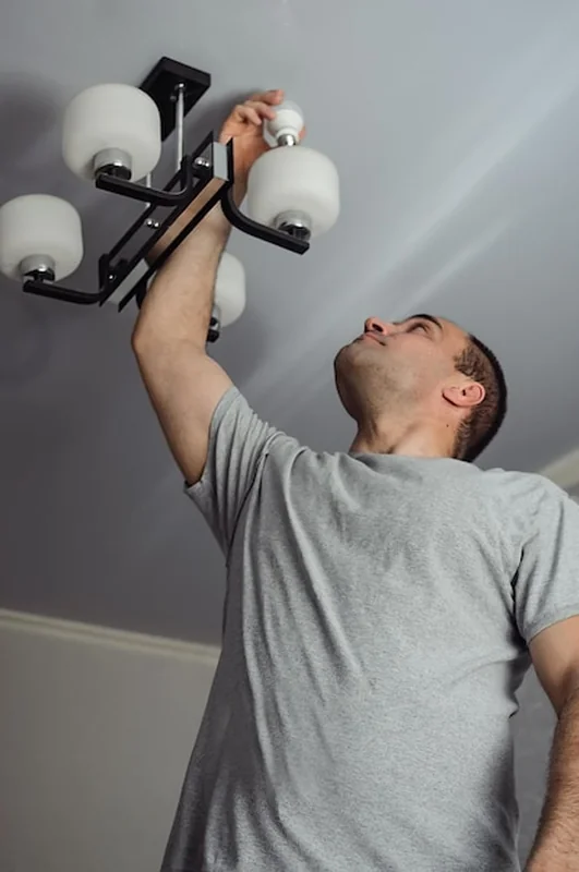 Mężczyzna wymienia żarówkę w żyrandolu