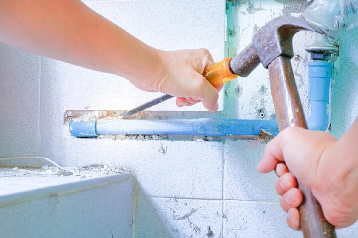 Pracownik usuwa płytkę ścienną i rurę