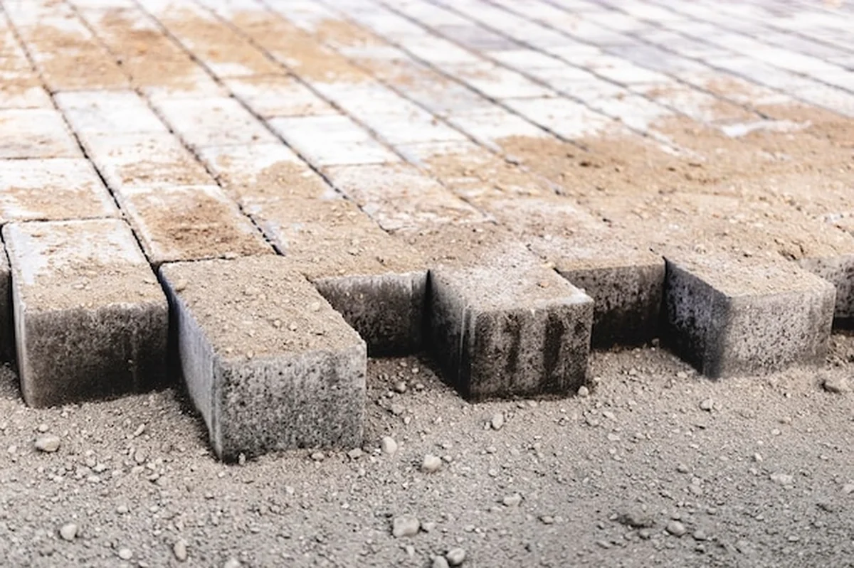 Układanie płyt chodnikowych na przygotowanej powierzchni z kostką w tle