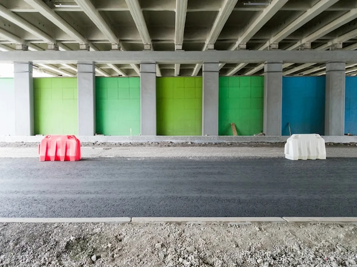 Remont drogi asfaltowej pod mostem ogrodzonej plastikowymi płotkami