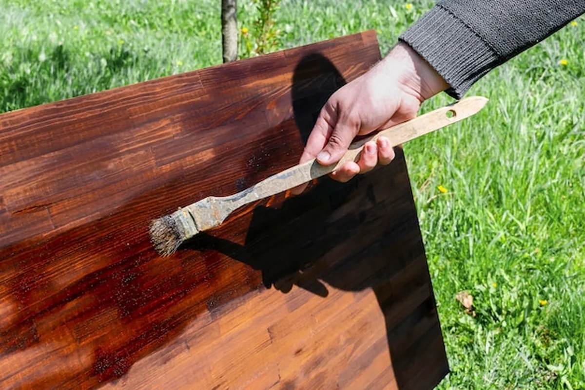 Mężczyzna maluje drewno brązową plamą pędzlem na stole