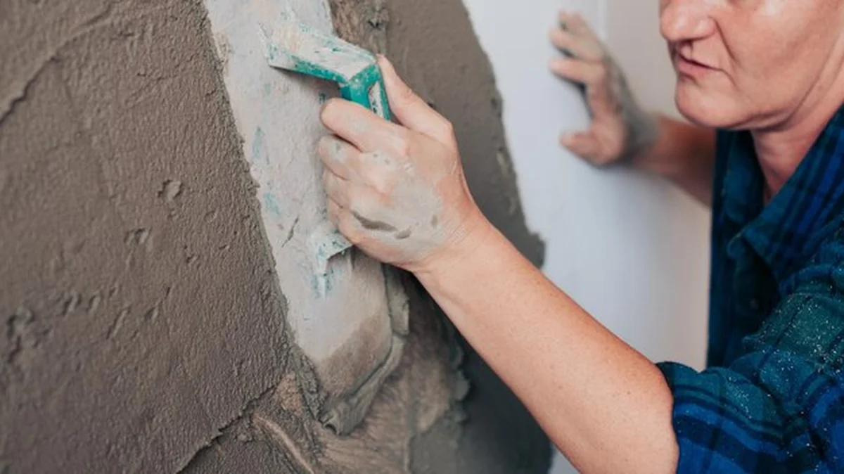 Osoba rozprowadzająca cement na ścianie przy użyciu kielni. Budowa ściany i aplikacja cementu w trakcie