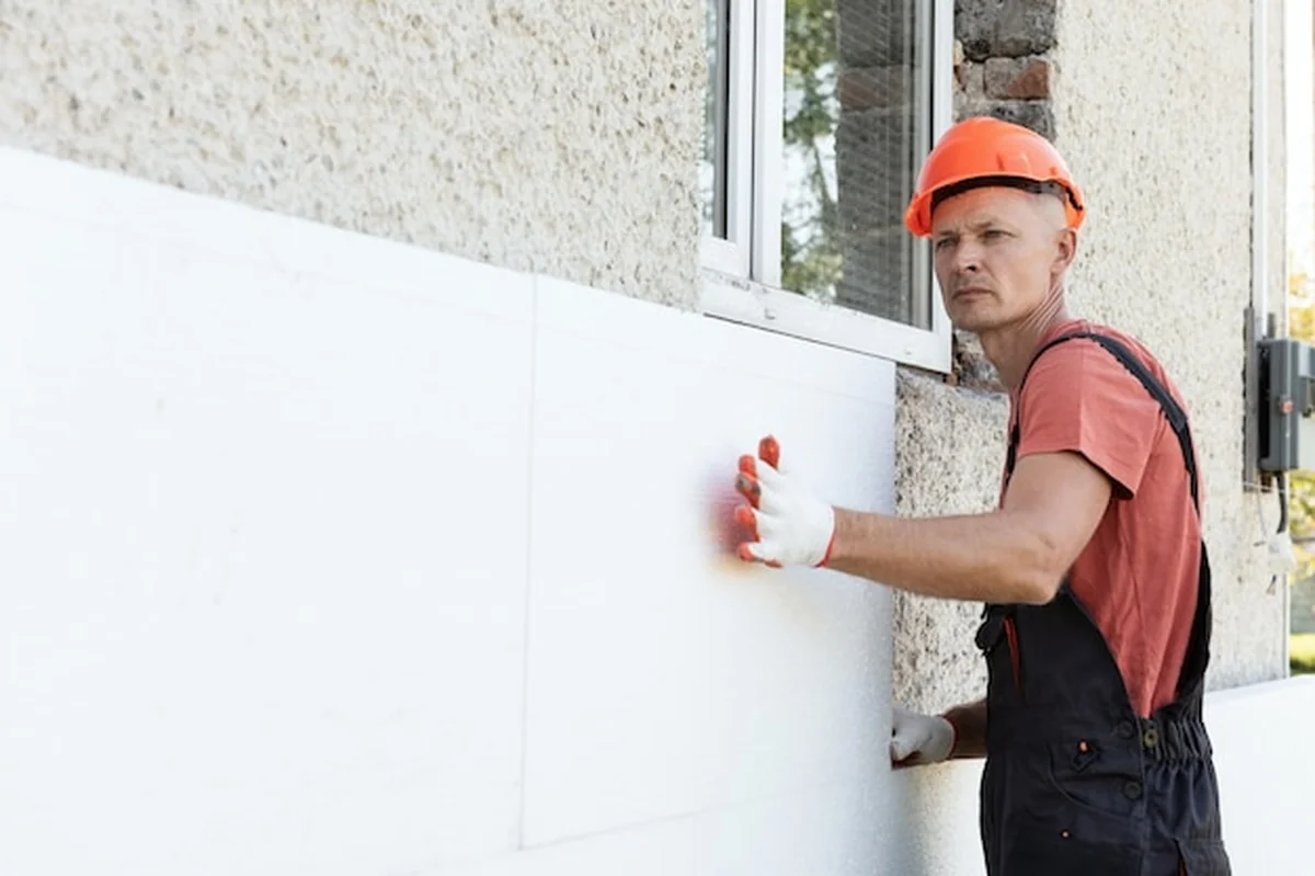 Pracownik montuje płytę styropianową na elewacji domu