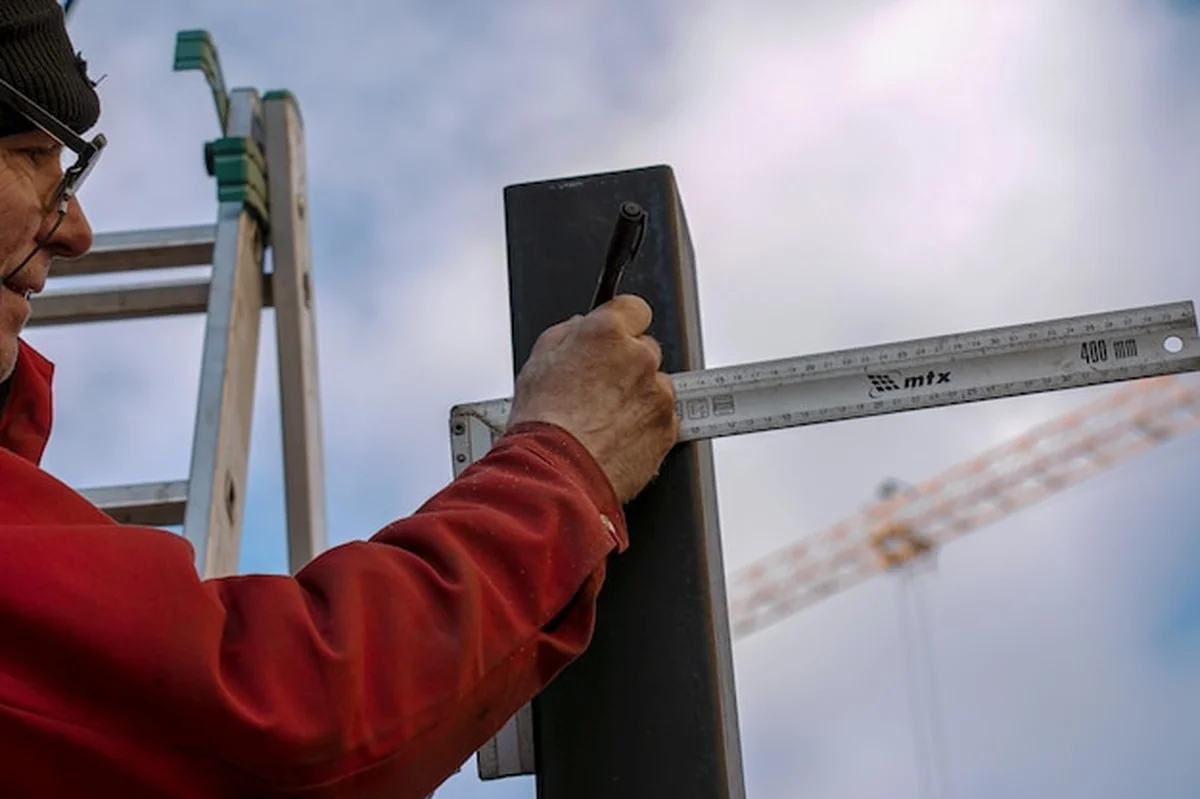 Robotnik mierzy kwadratową rurę żelazną linijką