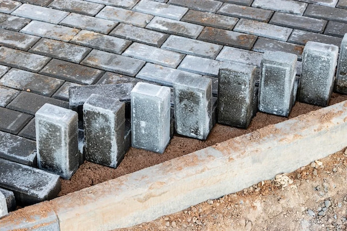 Układanie płyt chodnikowych na przygotowanej powierzchni z kostką w tle