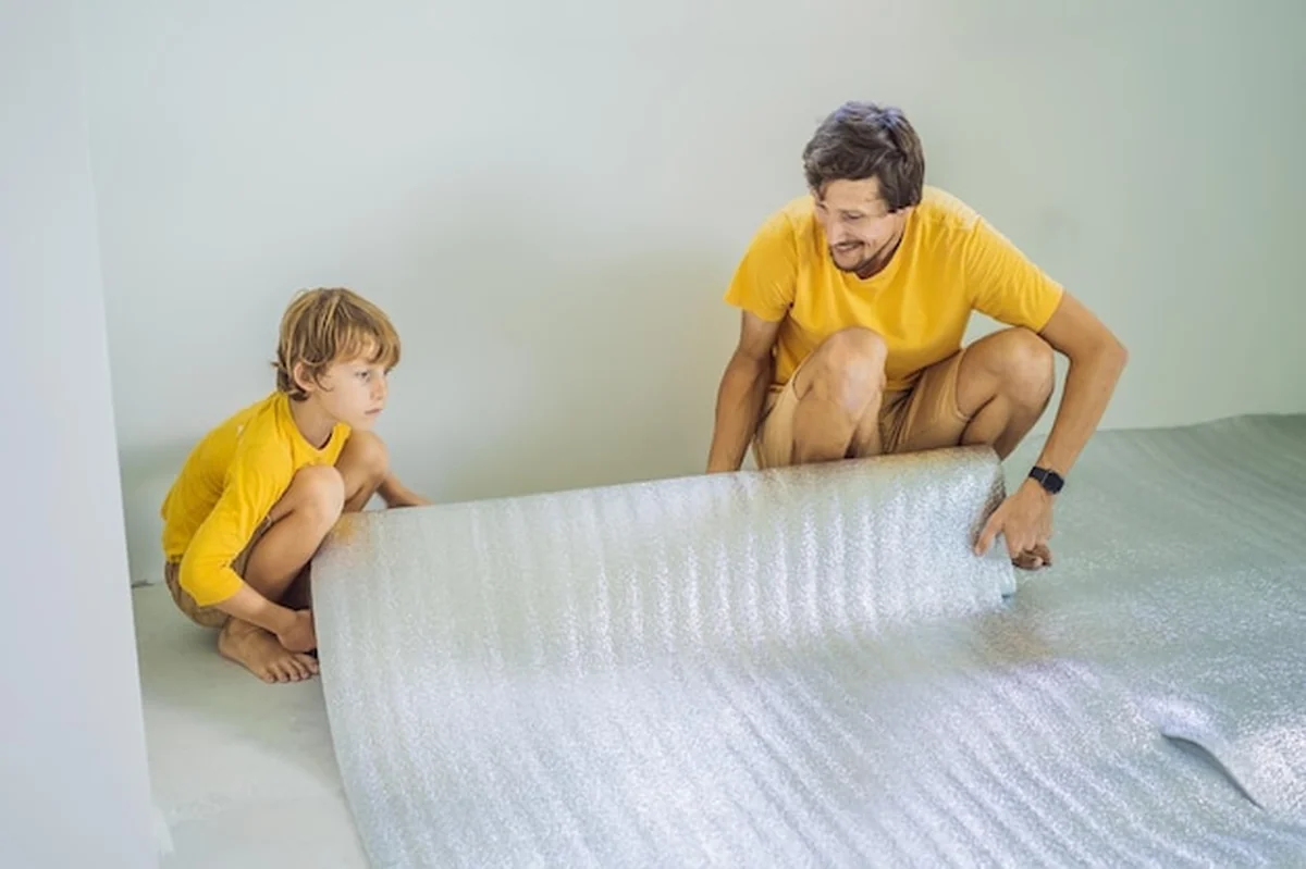 Ojciec i syn kładą izolację podłogową przed montażem podłogi laminowanej drewnianej