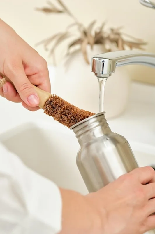 Kobieta myje metalową butelkę kokosową szczotką