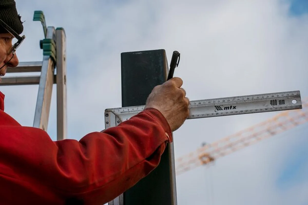 Robotnik mierzy linijką kwadratową rurę