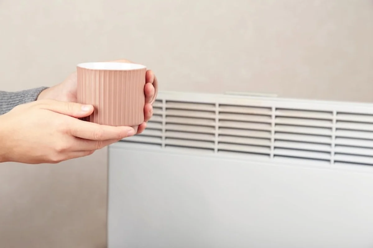Kobieta z filiżanką herbaty przy elektrycznym grzejniku w domu