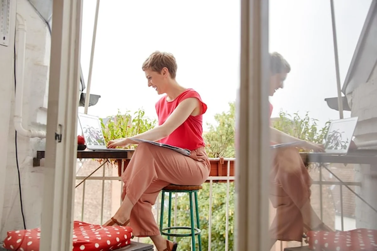 Szczęśliwa kobieta siedząca na balkonie z laptopem i mapą